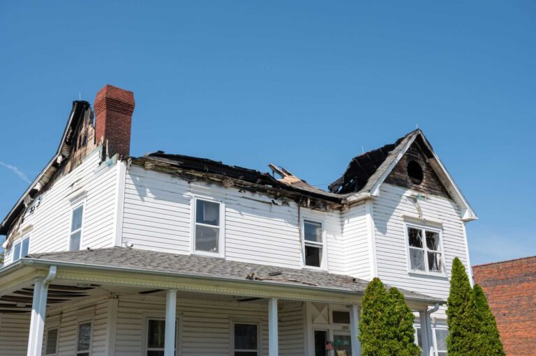 Fire-damaged two-story home with burned roof, charred siding, and visible structural damage requiring restoration and repair.